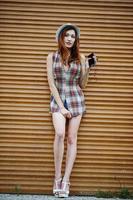 Amazing long legs with hig heels girl wear on hat against shutter listening music from headphones of mobile phone. photo