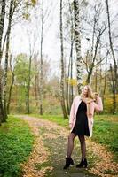 Young blonde girl at pink coat posed on autumn park. photo