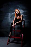 Fashion model red haired girl with originally make up like leopard predator against steel wall. Studio portrait on ladder. photo