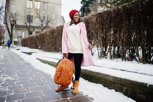 African american girl in red hat and pink coat with backpack at street of city on winter day. photo