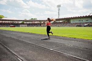 chica deportiva fitness en ropa deportiva en el estadio de deportes al aire libre. mujer sexy feliz corriendo en la caminadora de atletismo en el estadio. foto