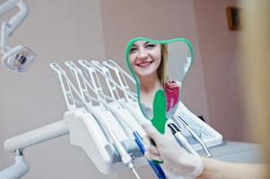 hermoso dentista mostrando los dientes nuevos de su paciente a través del espejo en el gabinete dental. foto