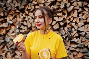 Young funny girl with bright make-up, wear on yellow shirt hold picece of orange against wooden background. photo