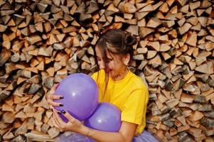 Young funny girl with bright make-up, wear on yellow shirt with colored balloons against wooden background. photo