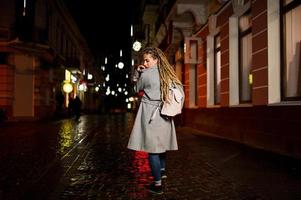 Girl with dreadlocks walking at night street of city. photo