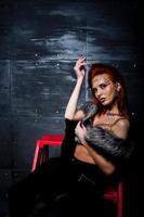 Fashion model red haired girl with originally make up like leopard predator against steel wall. Studio portrait on ladder. photo