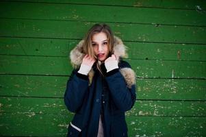 hermosa chica morena en ropa de abrigo de invierno. modelo en chaqueta de invierno sobre fondo de madera verde. foto