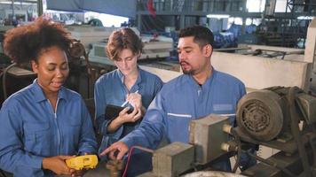 multiracial professionella industriingenjörsteam i säkerhetsuniformer arbetar genom att inspektera maskinernas spänningsström, kontrollera och underhålla elsystemserviceyrken vid tillverkningsfabriken. video