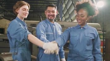 multiraciale industriearbeiders in veiligheidsuniformen werken samen met eenheid, slaan de handen ineen en drukken gelukkig werk uit samen met een glimlach en vrolijk in een mechanische fabriek, professionele ingenieursbezetting. video