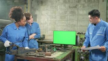 tre multiracial professionella industriingenjörsarbetarteam i säkerhetsuniformer metallarbete diskuterar nära grön skärmmonitor, mekaniska svarvmaskiner och verkstad i tillverkningsfabriken. video