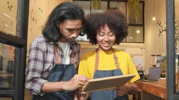 Zwei junge Startup-Barista-Partner mit Schürzen stehen an der Tür eines ungezwungenen Cafés, schreiben an Bord und zeigen ein offenes Schild, ein fröhliches und fröhliches Lächeln mit Jobs im Café-Service und neue Unternehmer. video