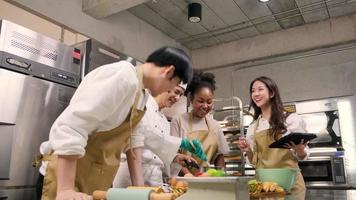 Hobby cuisine course, senior male chef in cook uniform teaches young cooking class students to prepare, mix and stir ingredients for pastry foods, fruit pies in restaurant stainless steel kitchen. video