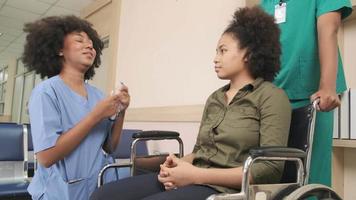 junge afroamerikanische ärztin mit stethoskop in uniform überprüft verletzungspatientenmädchen im rollstuhl im ambulanten unfallklinikkrankenhaus, krankheitsmedizinische klinikuntersuchung, gesundheitshalle. video