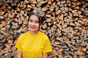 jovencita divertida con maquillaje brillante, como princesa de cuento de hadas, vestida con camisa amarilla y corona sobre fondo de madera. foto