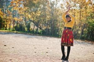 African american girl at yellow and red dress at golden autumn fall park. photo