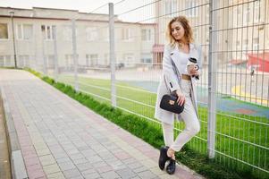 Stylish curly blonde model girl wear on white posing against fence. photo