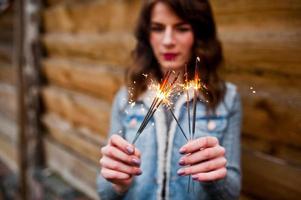 Portrait of brunette girl in jeans jacket with bengal lights in hands. photo