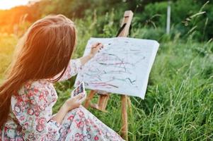 Portrait of a gorgeous happy young woman in beautiful dress sitting on the grass and painting on paper with watercolors. photo