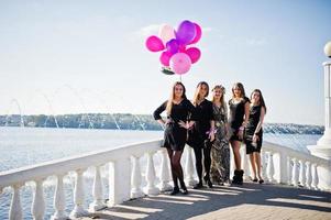 cinco chicas visten de negro caminando con globos en una despedida de soltera contra el lago. foto