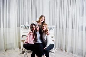 Four cute friends girls wear on warm sweaters and black pants against old piano with christmas decoration at white room. photo