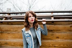 Portrait of brunette curly girl in jeans jacket against wooden wall. photo