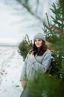 Portrait of gentle girl in gray coat and hat against new year tree outdoor. photo