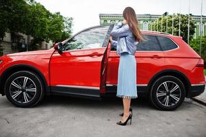 foto al aire libre de una mujer hermosa posando cerca de un auto todoterreno naranja.