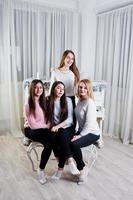 Four cute friends girls wear on warm sweaters and black pants against old piano with christmas decoration at white room. photo