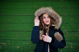 Beautiful brunette girl in winter warm clothing. Model on winter jacket against green wooden background. photo