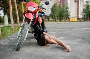 retrato de una mujer genial e impresionante con chaqueta de cuero negro sentada junto a una bicicleta roja genial. foto