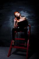 Fashion model red haired girl with originally make up like leopard predator against steel wall. Studio portrait on ladder. photo