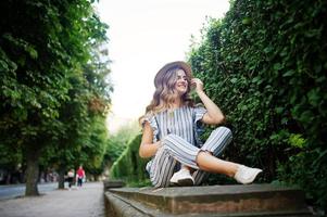 retrato de una mujer joven impresionante en general a rayas sentada en el parque y escuchando la música con los auriculares puestos. foto