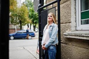 chica rubia vestida con chaqueta de jeans con mochila posada en las calles de la ciudad. foto