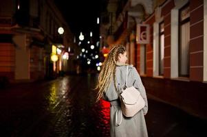 chica con rastas caminando por la calle de noche de la ciudad. foto
