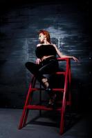 Fashion model red haired girl with originally make up like leopard predator against steel wall. Studio portrait on ladder.