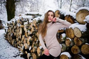 Beautiful brunette girl in winter warm clothing. Model on winter sweater near stump. photo