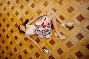 Portrait of a stunning young woman in gorgeous dress laying on the floor with her smartphone. photo