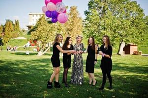 cinco chicas visten de negro con globos bebiendo champán rojo en la despedida de soltera. foto