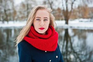 Portrai of blonde girl in red scarf and coat against frozen lake on winter day. photo