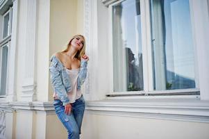 Blonde girl wear on jeans posed against old house. photo