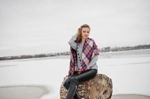 Curly blonde girl in checkered plaid against frozen lake at winter day. photo