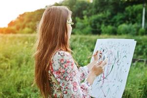 Portrait of an attractive young woman in long dress painting with watercolor in nature. photo