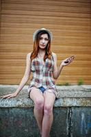 Amazing long legs with hig heels girl wear on hat against shutter listening music from headphones of mobile phone. photo