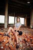 Girl wear on shorts at abadoned factoty sitting on brick. photo