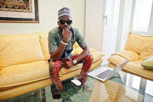 Rich african man sitting on sofa at his appartment and working on notebook. photo