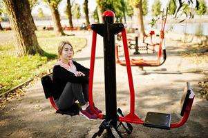 la joven tiene el entrenamiento y hace ejercicio al aire libre en simuladores callejeros. deporte, fitness, concepto de entrenamiento callejero. foto