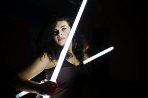 Curly brunette plus size model with two long led lamp at black room. photo