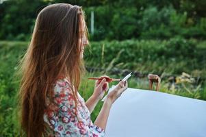 Portrait of an attractive young woman in long dress painting with watercolor in nature. photo