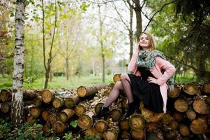 joven rubia con abrigo rosa posada sobre fondo de tocones de madera. foto
