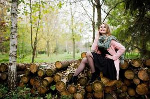 Young blonde girl at pink coat posed against wooden stumps background. photo